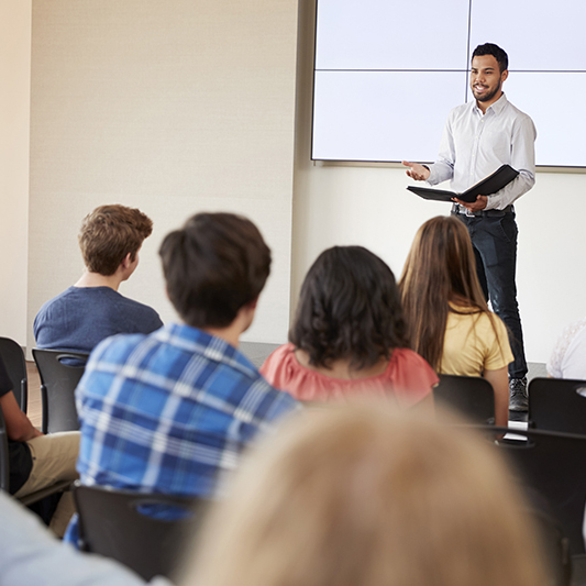 Teacher Giving Presentation To High School Class In Front Of Screen